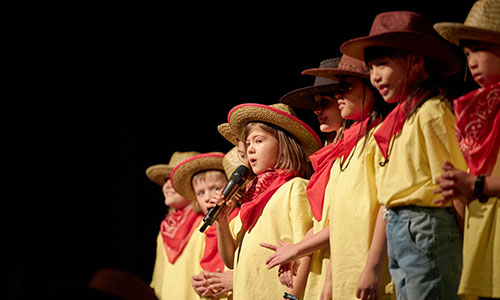 Students singing on the stage wearing cowboy dresses