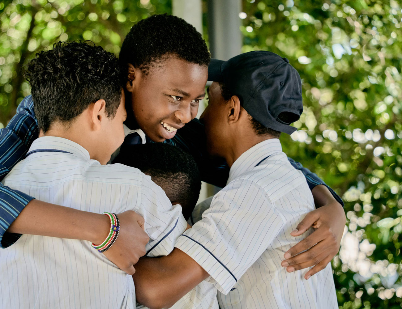Secondary male student hugging three male Middle School students